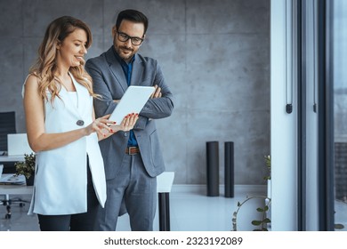 Image of two colleagues discussing about new project. Shot of a young businessman and businesswoman using a digital tablet together in an office. Business colleagues in modern office using tablet - Powered by Shutterstock