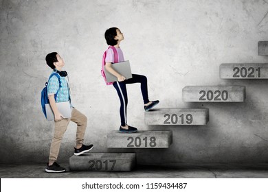 Image of two elementary students holding laptop while stepping together on the stair toward number 2019