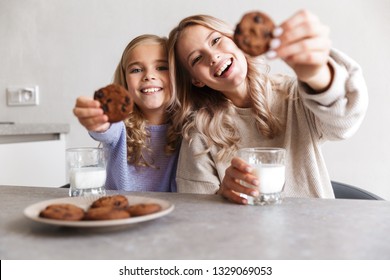 Image of two happy girls sisters at kitchen indoors eat have a breakfast together.