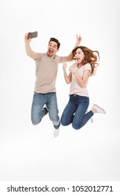 Image Of Two Happy People Man And Woman Having Fun And Making Selfie On Cell Phone While Jumping Together Over White Background