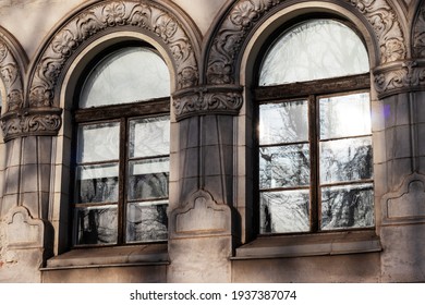 The image of two symmetrical windows whose frames have a special architecture and in which the trees outside are reflected