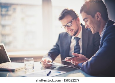 Image two young businessmen using touchpad at meeting