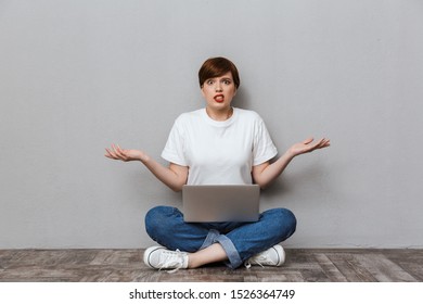 Image Of Uptight Woman Sitting On Floor And Using Laptop Computer Isolated Over Gray Background