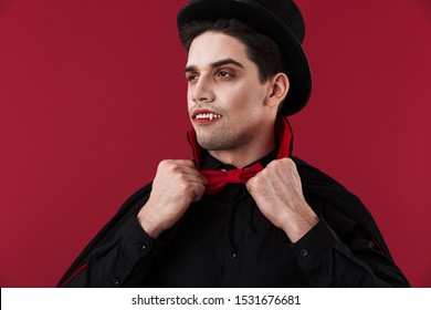 Image Of Vampire Man With Blood And Fangs In Black Halloween Costume Touching His Bow Tie Isolated Over Red Wall