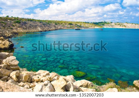 Image with a view of a bay near Cape Greco, Cyprus. Rock coastline near deep green transparent emerald water against a rocky hill. Amazing cloudscape. Warm day in fall