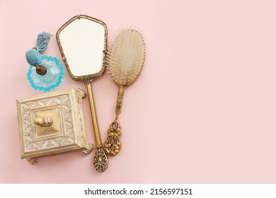 Image Of Vintage Hair Comb, Perfume Bottle And Hand Mirror Over Pastel Pink Background