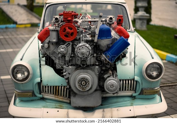 Image of a vintage tuned car, with a large engine\
sticking out of its hood.