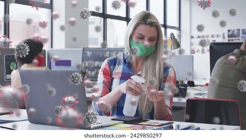 Image of virus cells over caucasian businesswoman wearing face mask and disinfecting hands. global networks, business, data processing and digital interface concept digitally generated image.