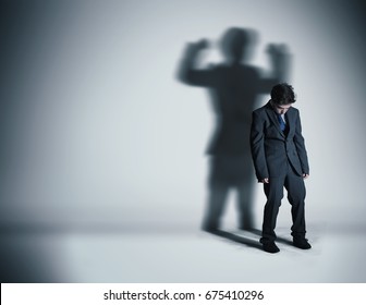 Image Of A Weak Businessman Standing Depressed In Front Of A Wall And His Shadow Shows Streght.