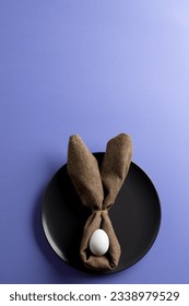 Image of white easter egg and bunny ears on black plate and copy space on purple background. Easter, religion, tradition and celebration concept.