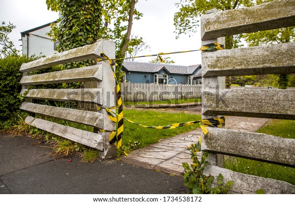 Image of a white picket fence made from triangles with\
yellow and black tape tied to the fence blocking anybody from\
entering the pub car park or beer garden due to government issued\
lockdown 