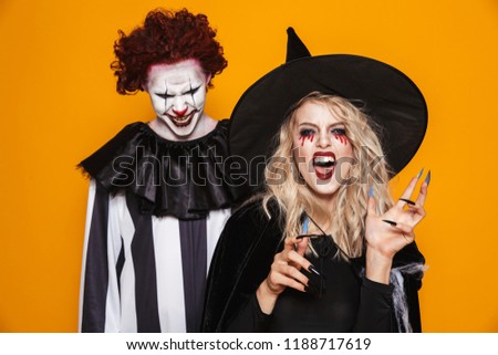 Image of witch woman and joker man wearing black costume and halloween makeup looking at camera isolated over yellow background