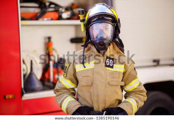 Image of woman firefighter in helmet and mask\
standing near fire truck