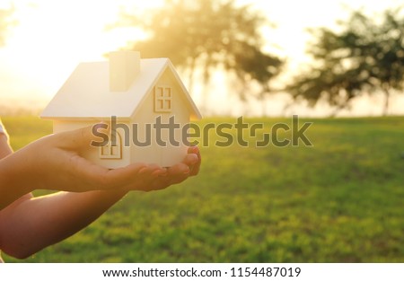 Image of woman holding small wooden house outdoors at sunset light