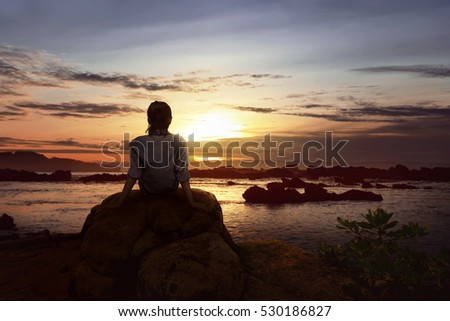 Image of woman sitting on the rock looking the sunset