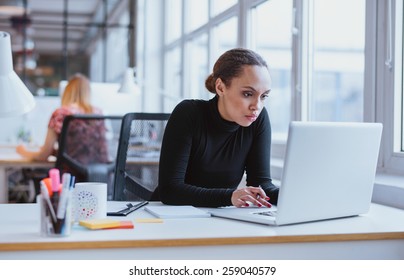 Image of woman using laptop while sitting at her desk. Young african american businesswoman sitting in the office and working on laptop.