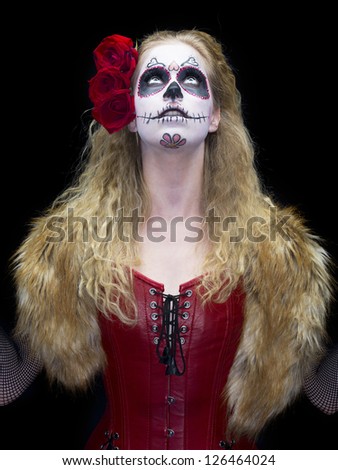 Image of a woman wearing traditional sugar skull make-up and looking up against black background.