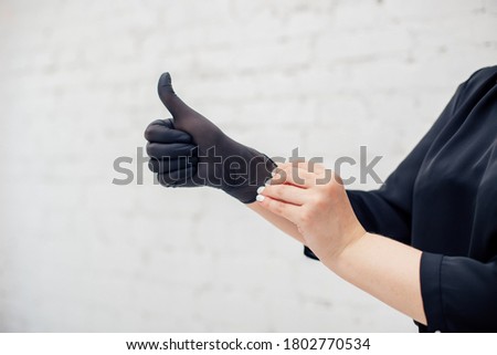 An image of a woman's hands putting on a black latex glove