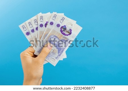 Image woman's hands which holds British pounds in her hands isolated over blue studio background