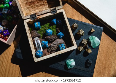 Image of a wooden box with blue role-playing game dice on top of a black notebook with green crystals and metal dice.