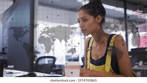 Image of world map, globe and data over biracial casual businesswoman using computer at office. Business, data, network, digital interface and global communication, digitally generated image.