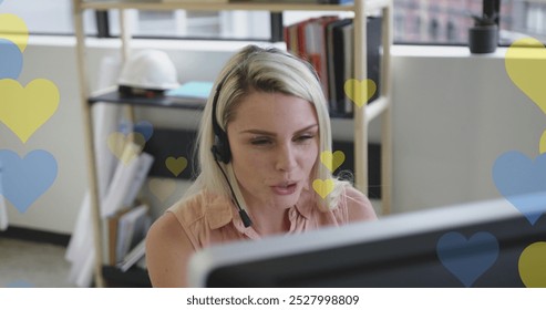 Image of yellow and blue hearts over caucasian businesswoman using phone headset. Ukraine crisis, social media, communication, business and data processing concept digitally generated image.