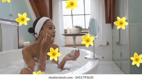 Image of yellow flowers over biracial woman relaxing in bath moisturising face at home. relaxation, health and wellbeing concept digitally generated image. - Powered by Shutterstock