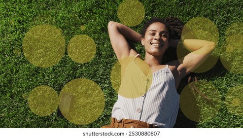 Image of yellow spots over smiling biracial woman lying in park. health and fitness concept digitally generated image. - Powered by Shutterstock