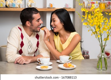 Image of a young adorable couple at a coffee shop, a girlfriend feeding her boyfriend with a tasty chocolate snack  - Powered by Shutterstock