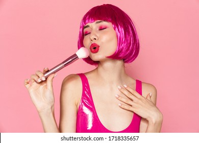 Image Of Young Amusing Girl Wearing Wig Making Fun With Powder Brush Isolated Over Pink Background