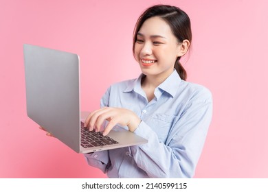 Image of young Asian business woman holding laptop on pink background