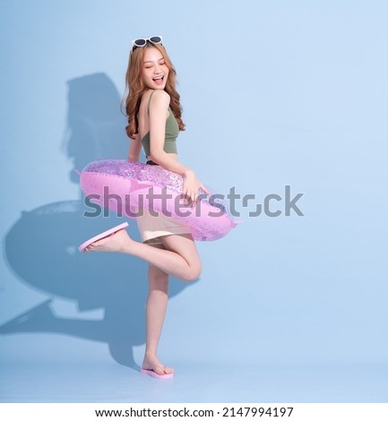 Image of young Asian girl holding swimming float on blue background, summer vacation concept