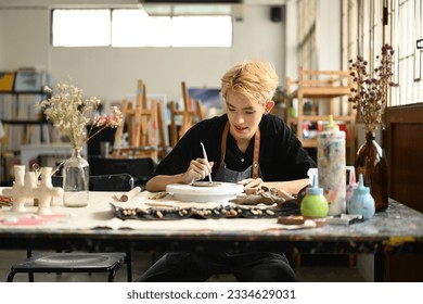 Image of young asian man enjoying creative process, creating handmade ceramics in pottery workshop - Powered by Shutterstock