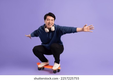 Image of young Asian man playing skateboard on purple background