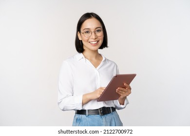 Imagen de una joven asiática, trabajadora de compañía con anteojos, sonriendo y sosteniendo una tableta digital, de pie sobre fondo blanco