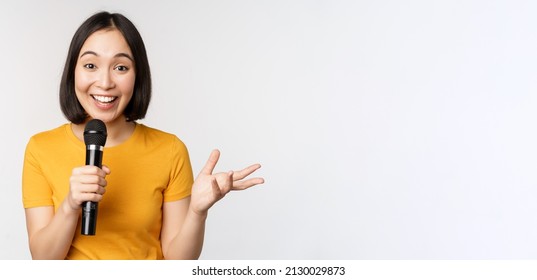 Image Of Young Asian Woman Talking In Microphone, Perfom With Mic, Giving Speech, Standing In Yellow Tshirt Against White Background