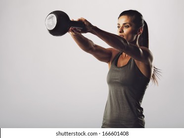 Image of young attractive female doing kettle bell exercise on grey background. Fitness woman working out. Crossfit exercise.