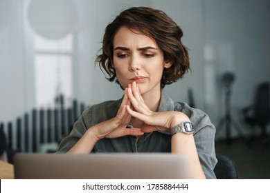 Image of young beautiful brooding woman working with laptop while sitting at table in office - Powered by Shutterstock