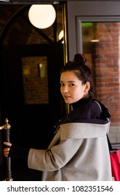 Image Of Young Beautiful Female Model Of Mixed Race Opening A Door Dressed In Gray Coat With Red Textile Bag.