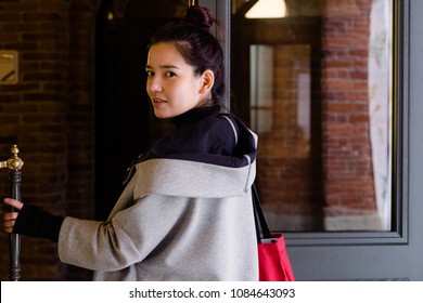 Image Of Young Beautiful Female Model Of Mixed Race Opening A Door Dressed In Gray Coat With Red Textile Bag.