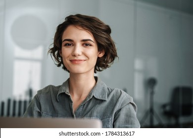 Bild einer jungen, wunderschönen Frau, die beim Arbeiten mit Laptop im Büro lächelt