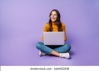 Image of young beautiful woman using laptop while sitting with legs crossed isolated over violet background - Powered by Shutterstock