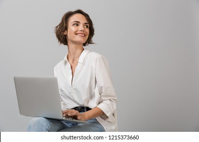 Image Of Young Business Woman Posing Isolated Over Grey Wall Background Sitting On Stool Using Laptop Computer.