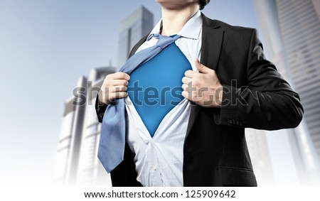 Image of young businessman showing superhero suit underneath his shirt standing against city background
