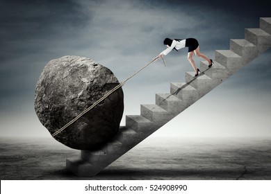 Image of a young businesswoman dragging a big stone while climbing up a stairway