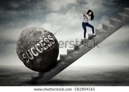 Image of young businesswoman pulling a boulder with success word while climbing on the stair
