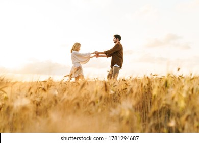 Image of young caucasian beautiful couple dancing together in golden field on countryside
