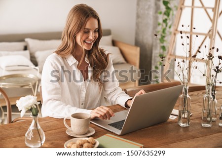 Image of young cheery happy positive cute beautiful business woman sit indoors in office using laptop computer.