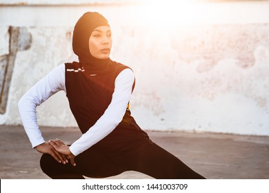 Image Of A Young Concentrated Muslim Sports Fitness Woman Dressed In Hijab And Dark Clothes Posing Make Sport Stretching Exercises Outdoors At The Street.