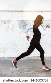 Image Of A Young Concentrated Muslim Sports Fitness Woman Dressed In Hijab And Dark Clothes Running Outdoors.